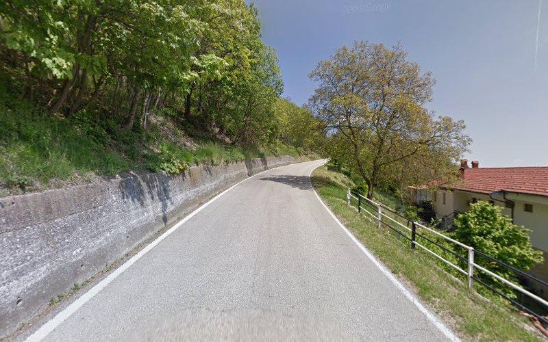 Una strada tortuosa fiancheggiata da alberi sulla sinistra e una casa con il tetto rosso sulla destra, sotto un cielo limpido.