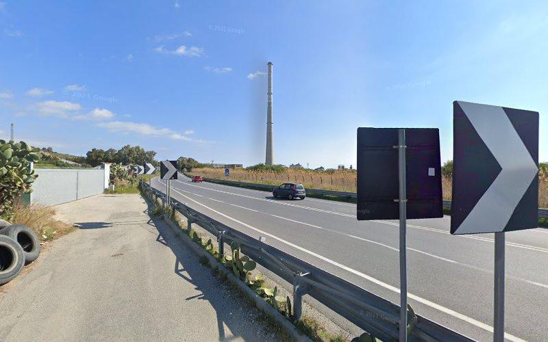 Un'autostrada con diverse auto che la percorrono. Il cielo è limpido e i segnali stradali con le frecce direzionali sono visibili sul lato destro dell'immagine. Sullo sfondo c'è un alto camino industriale.