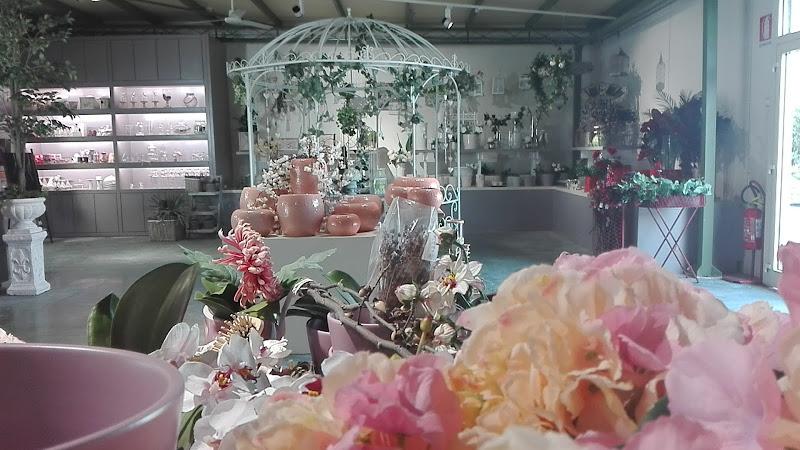 L'interno di un negozio di fiori con varie piante in vaso, fiori e oggetti decorativi. Scaffali ed espositori sono organizzati con i prodotti e un arco bianco da giardino è decorato con viticci e fiori pendenti.