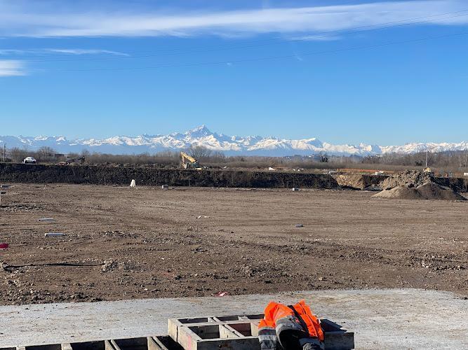 Cantiere con dispositivi di sicurezza arancioni in primo piano e montagne innevate sullo sfondo sotto un cielo azzurro e limpido.