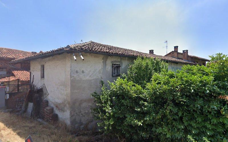 Un vecchio edificio usurato dal tempo con un tetto di tegole e cespugli cresciuti troppo sul lato in una zona rurale. Vari oggetti sono accatastati contro il muro esterno.