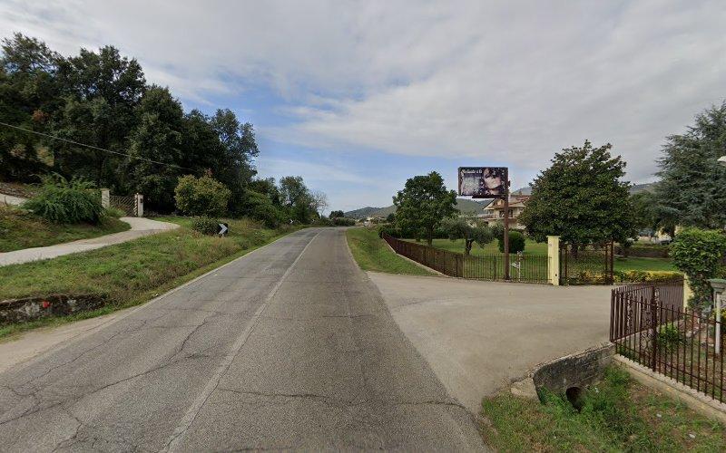 Una strada asfaltata fiancheggiata da verde e case, che conduce a un orizzonte lontano sotto un cielo parzialmente nuvoloso. Un cartellone pubblicitario è visibile sul lato destro vicino a un vialetto.