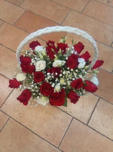 Un cesto di vimini bianco pieno di fiori rossi e bianchi, tra cui rose e gypsophila, adagiato su un pavimento piastrellato.